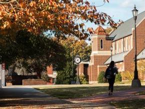 A student with their back to the camera walks on campus on a fall day